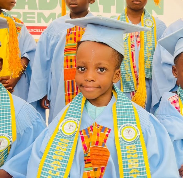 A smiling ASMA graduate in cap, gown and kente sash